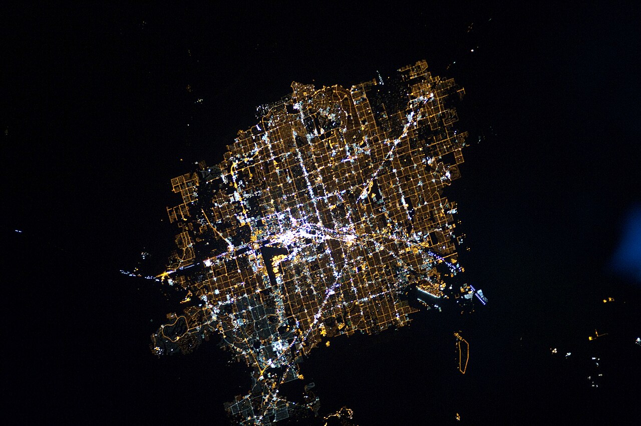 The Las Vegas valley photographed at night from the International Space Station: a dense grid of orange street lights filling the desert basin, with the brighter white line of the Strip running through the middle.